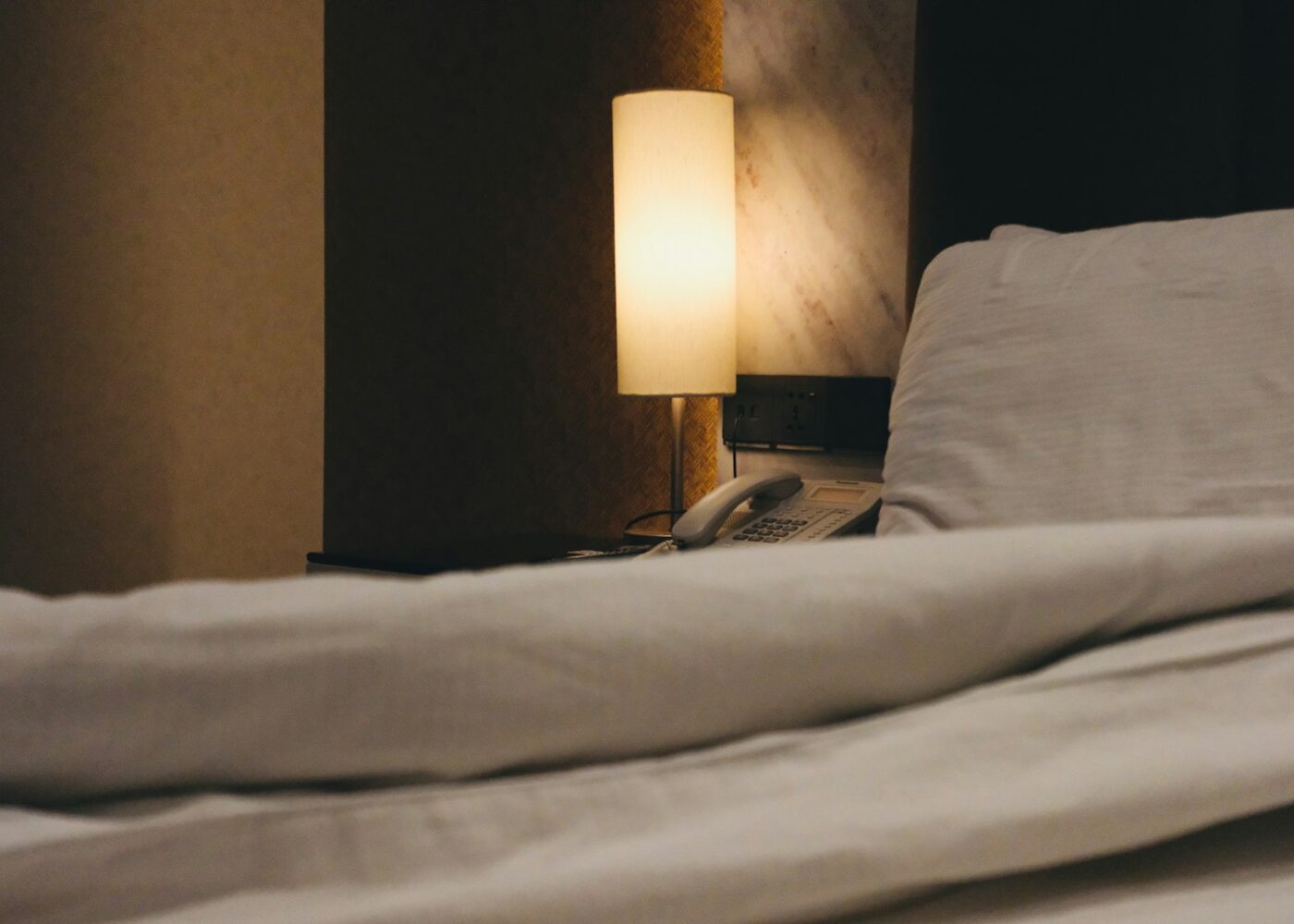 Prigu&scaron;ena noćna lampa pored kreveta sa bijelim pokrivačem &mdash; magnezijum i san